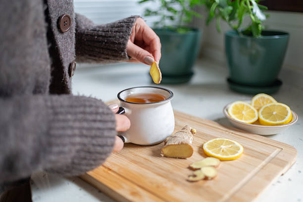 woman putting a slice of ginger in cup of tea at home